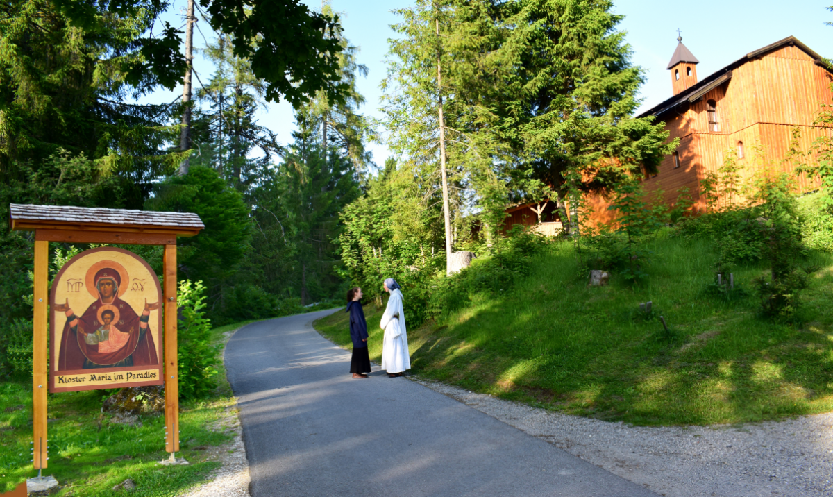 Auf dem Foto sieht man links am Wegrand eine große, mit einem kleinen Schindeldach überdachte Ikone der Mutter Maria mit dem Jesuskind, darunter die Aufschrift 