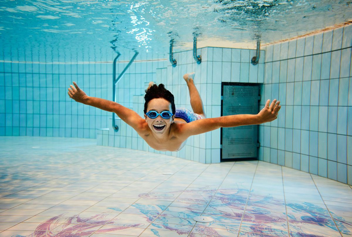 Kind mit Taucherbrille taucht im Becken. Der Boden ist bunt bemalt.