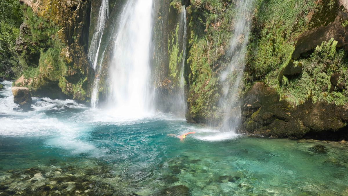 Mann schwimmt unter einem Wasaserfall.