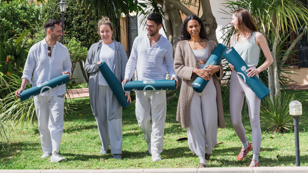 5 Personen gehen auf einer Wiese mit Yogamatten in der Hand.