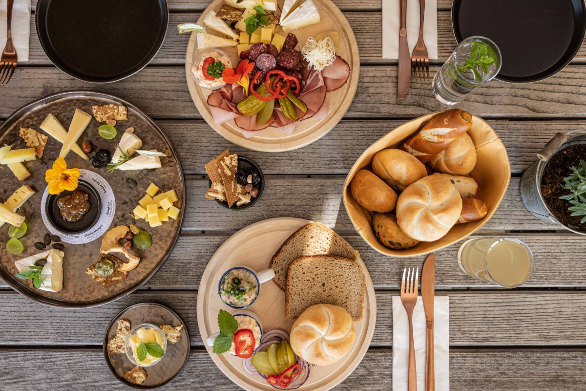 Jause mit Käse, Speck, Brot auf mehreren Tellern verteilt von ober fotografiert.