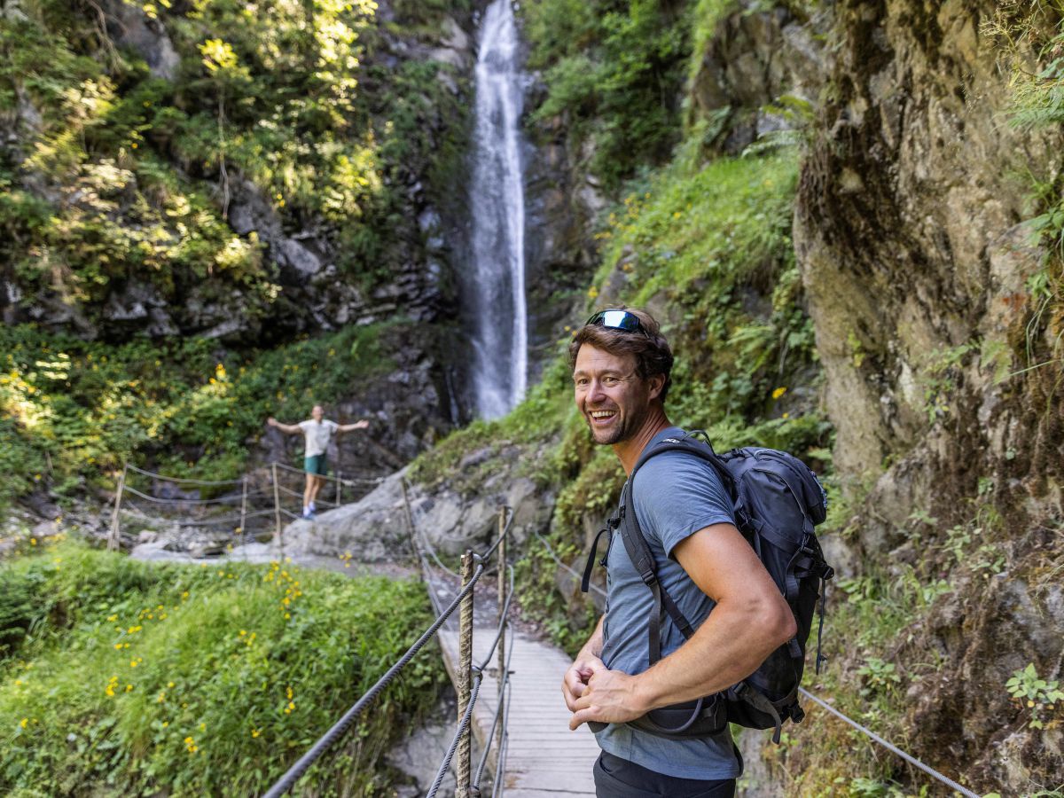 Mann und Frau auf einem Wanderweg zu einem Wasserfall.
