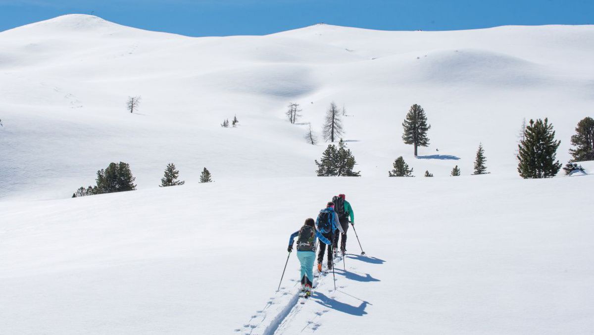 3 Personen mit Schiern aus einer unberührten schneebedeckten Hochebene.