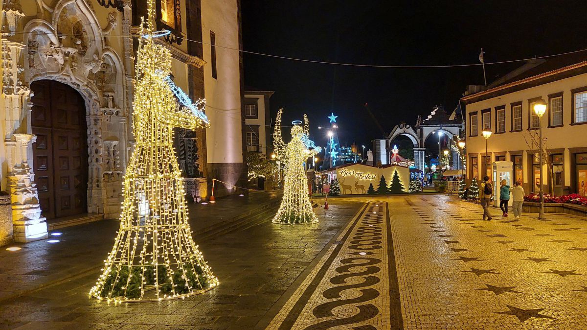 Nächtlich beleuchteter Platz mit 2 meterhohen Engeln aus Lichterketten vor dem Portal einer Kirche.