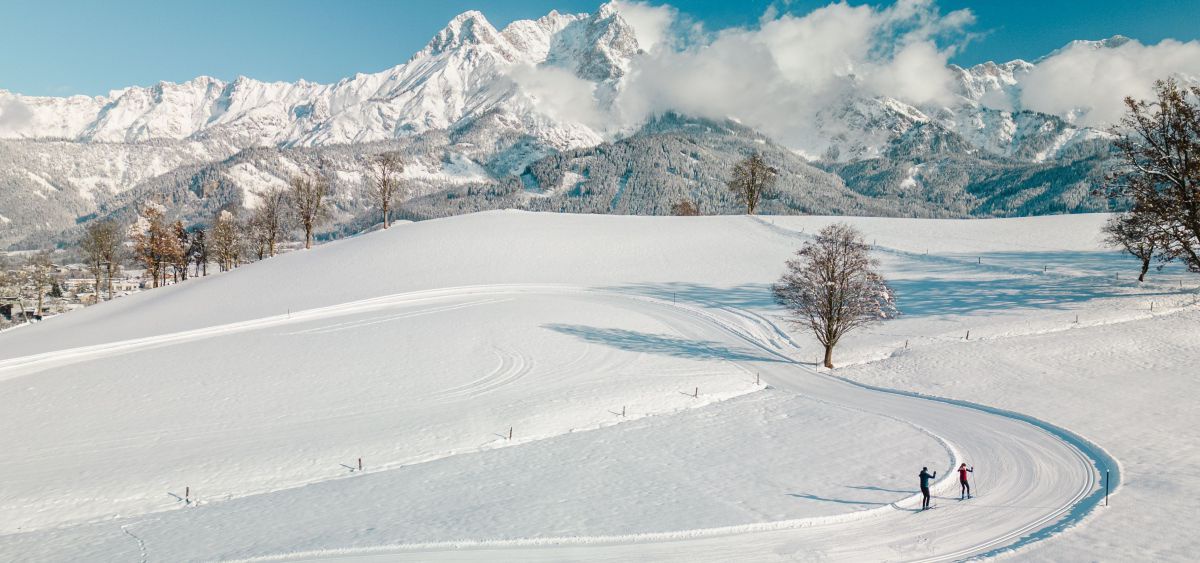 2 Langläufer auf der Loipe. Im Hintergrund verschneite Berglandschaft.