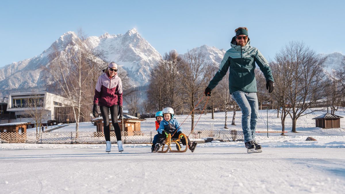 Mann und Frau mit Eislaufschuhen. Mann zieht 2 Kinder auf einem Schlitten.