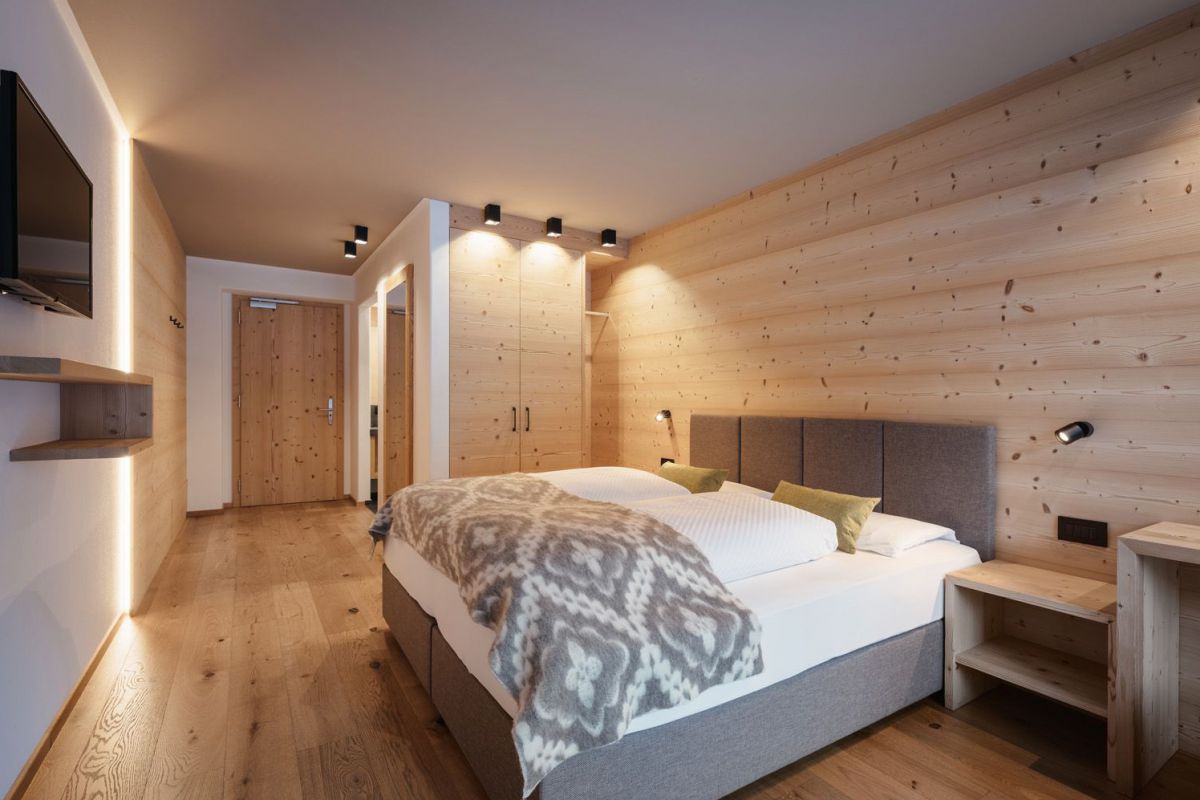 Zimmer mit Doppelbett. Wand hinter Bett und Boden sind aus Holz.