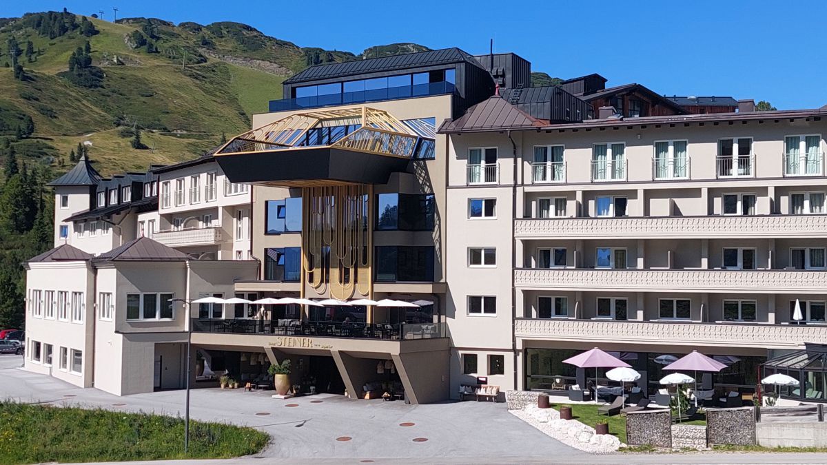 Aussenansicht des Hotels im Sommer.In der Mitte des Hauses kragt über dem Eingang oben im dritten Stück ein Pool aus der Fassade.
