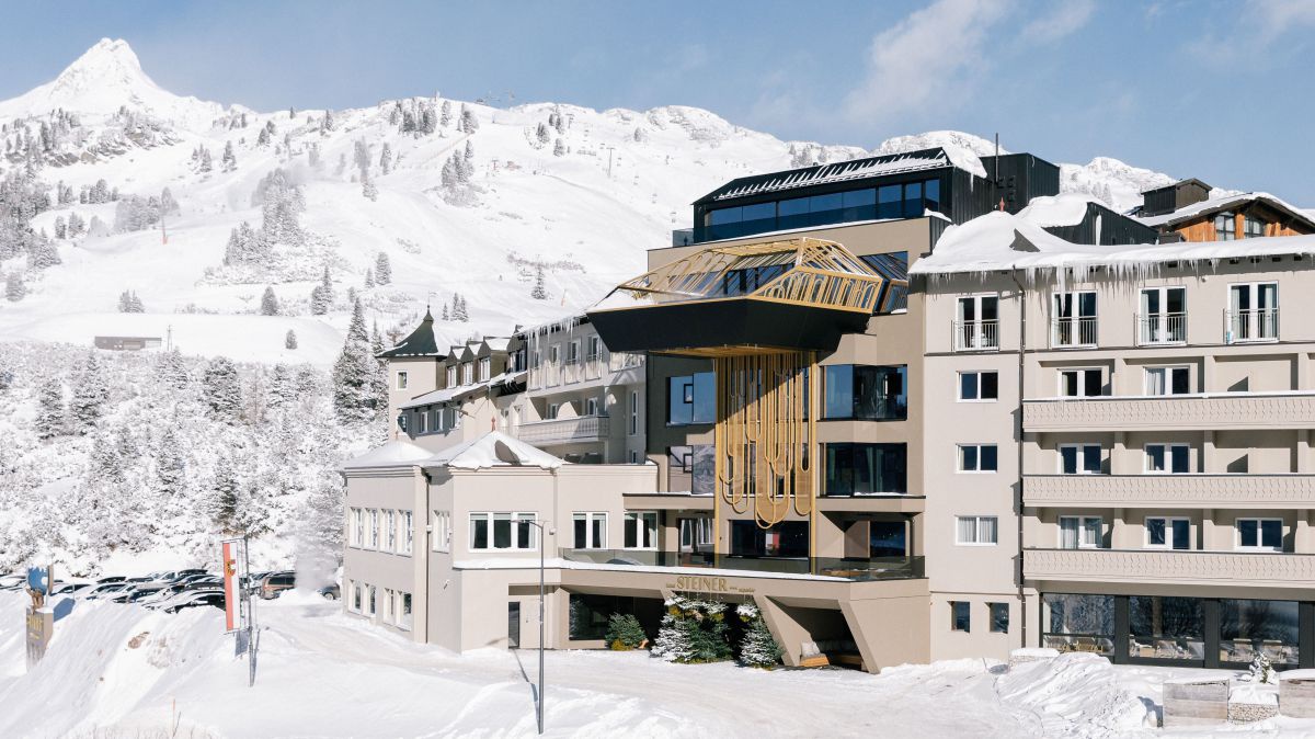 Aussenansicht des Hotels im Winter. Die Landschaft rundherum ist tief verschneit. In der Mitte des Hauses kragt über dem Eingang oben im dritten Stück ein Pool aus der Fassade. 