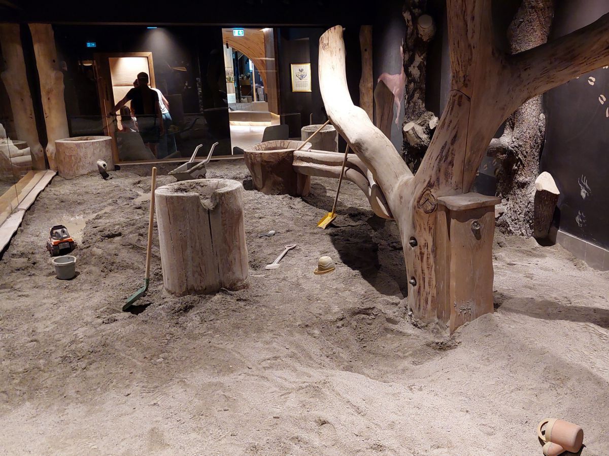 Sandspielplatz mit Holzstock und Baumstamm.
