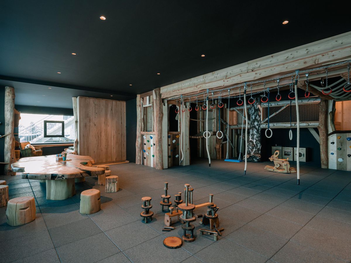 Raum mit großem Holztisch, rundherum Holzhocker, dahinter Klettergeräte, Puppentheater, Raum zum Verstecken uvm.