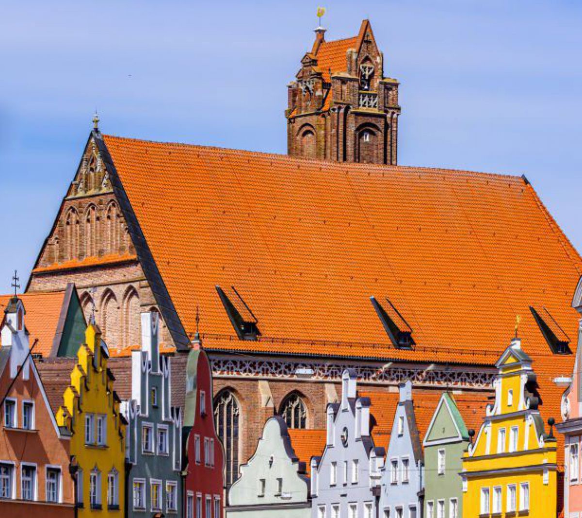 Häuserzeilen in der Altstadt von Landshut: Jedes Haus ist in einem anderen, meist pastelligen Farbton gestrichen (Gelb, Blau, Lachs, Rot, Grün,...) und jeder Dachgiebel ist individuell geformt. Die ziegelroten Dächer heben sich in starkem Kontrast vom bla