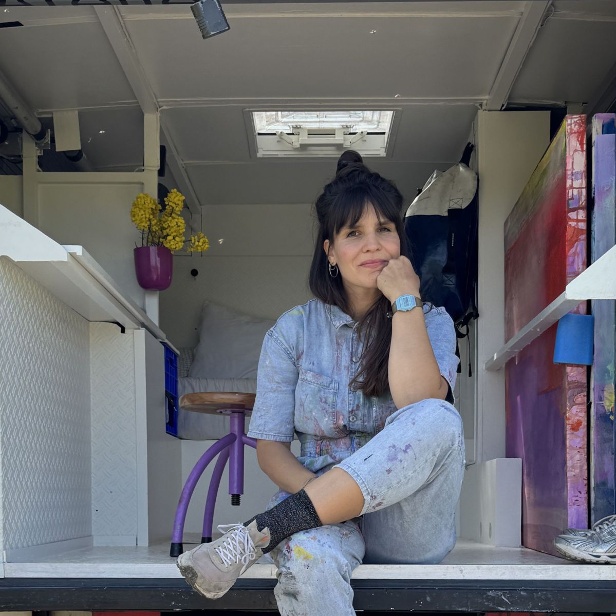 Eine Frau mit dunklen, langen Haaren und Stirnfransen sitzt auf der Ladefläche eines roten LKW. Hinter ihr sieht man das zu einem Wohnraum umgebaute Innere des alten Feuerwehrautos.