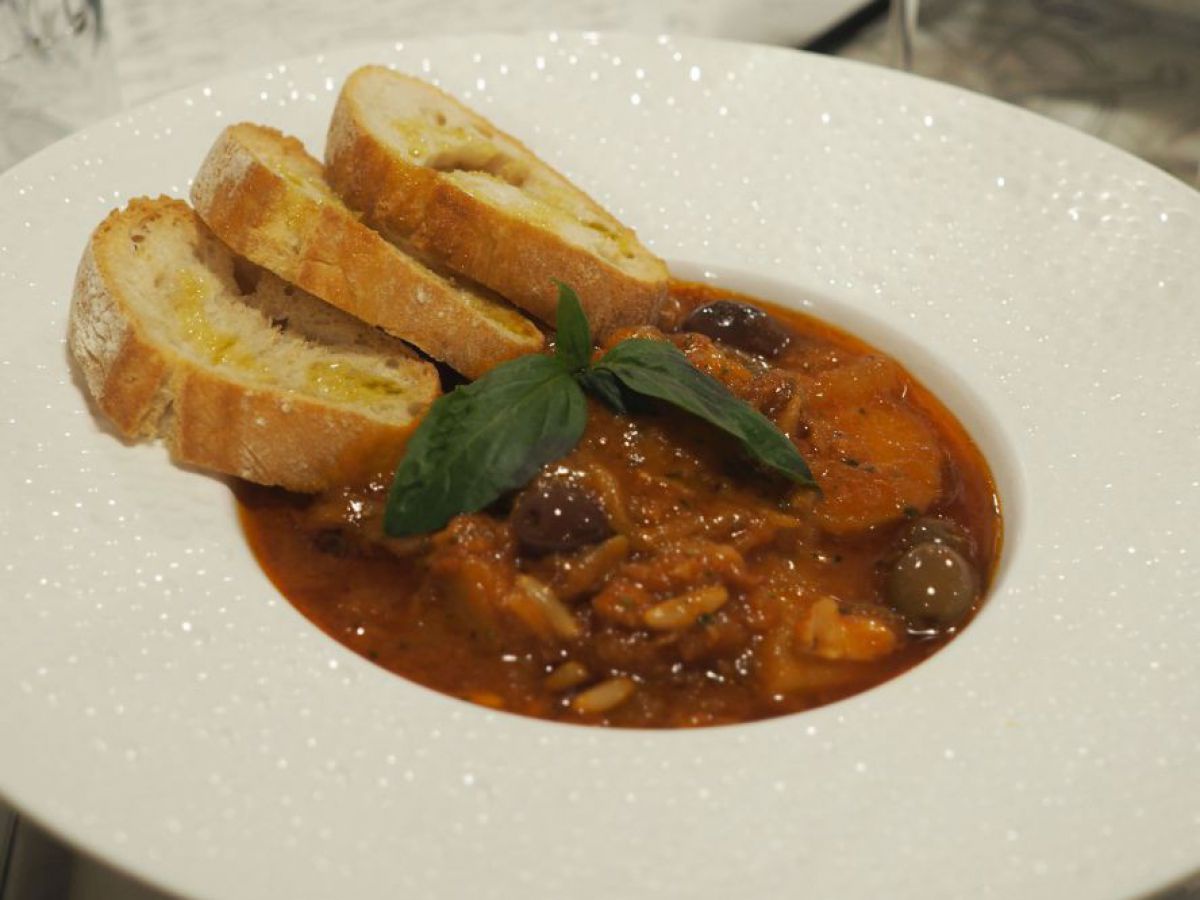 In einem weißen Suppenteller ist ein Fischgericht mit drei Scheiben Weißbrot angerichtet. 