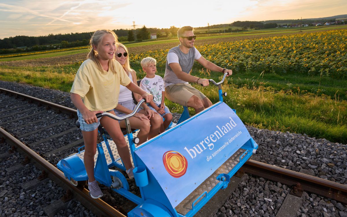 Familie auf einer blauen Draisine auf Bahngeleisen.