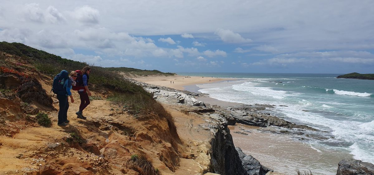 2 Frauen auf einem Weg etwas oberhalb eines Sandstrandes.