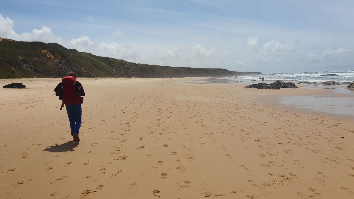 Frau mit Rucksack marschiert am Strand entlang.