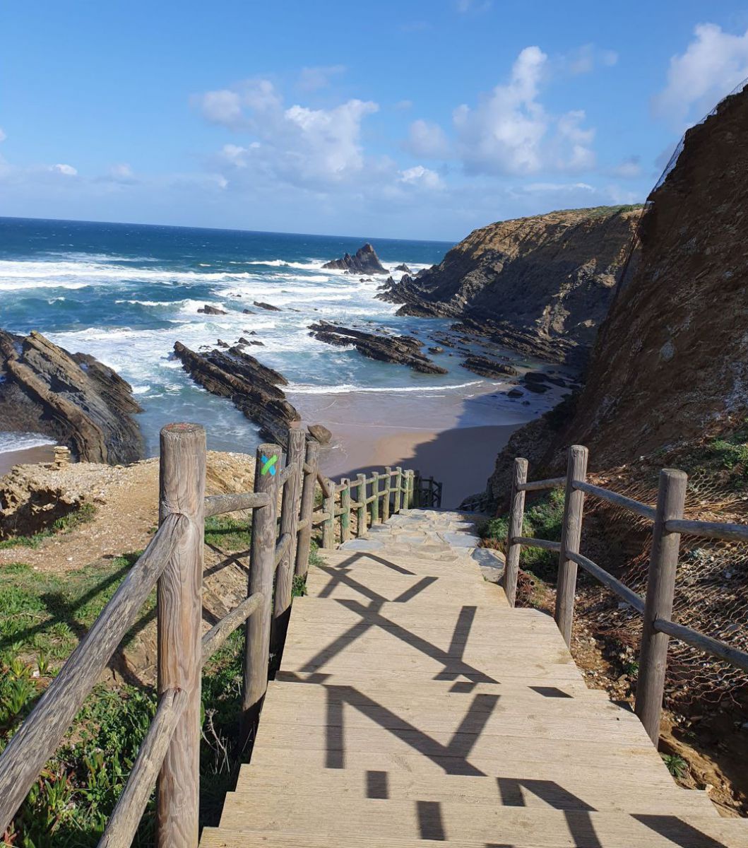 Holzstufen führen hinunter zu einem kleinen Sandstrand.