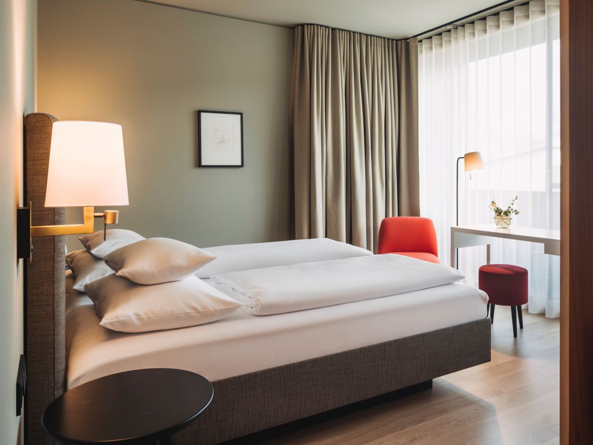 Blick in ein Zimmer mit Doppelbett, roten Sofas, rundes Nachtkästchen.