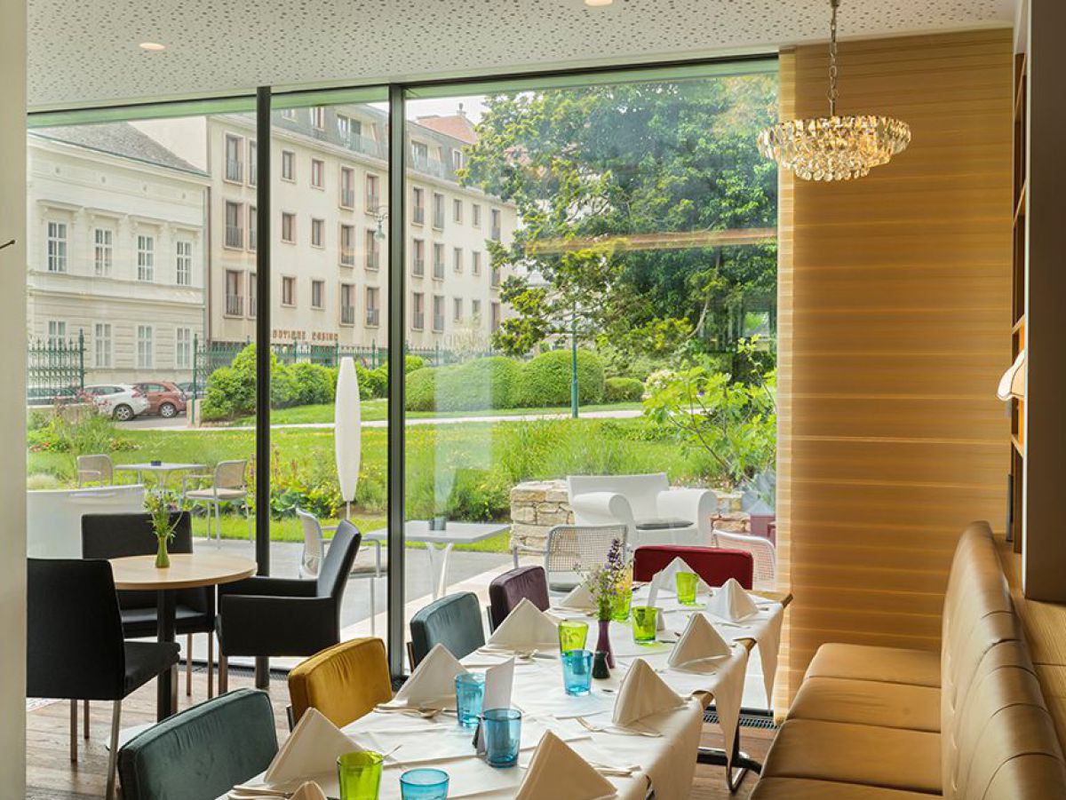 Frühstücks- und Speiseraum mit großer Glasfläche nach außen in den Park. Ein länglicher Tisch ist gedeckt.