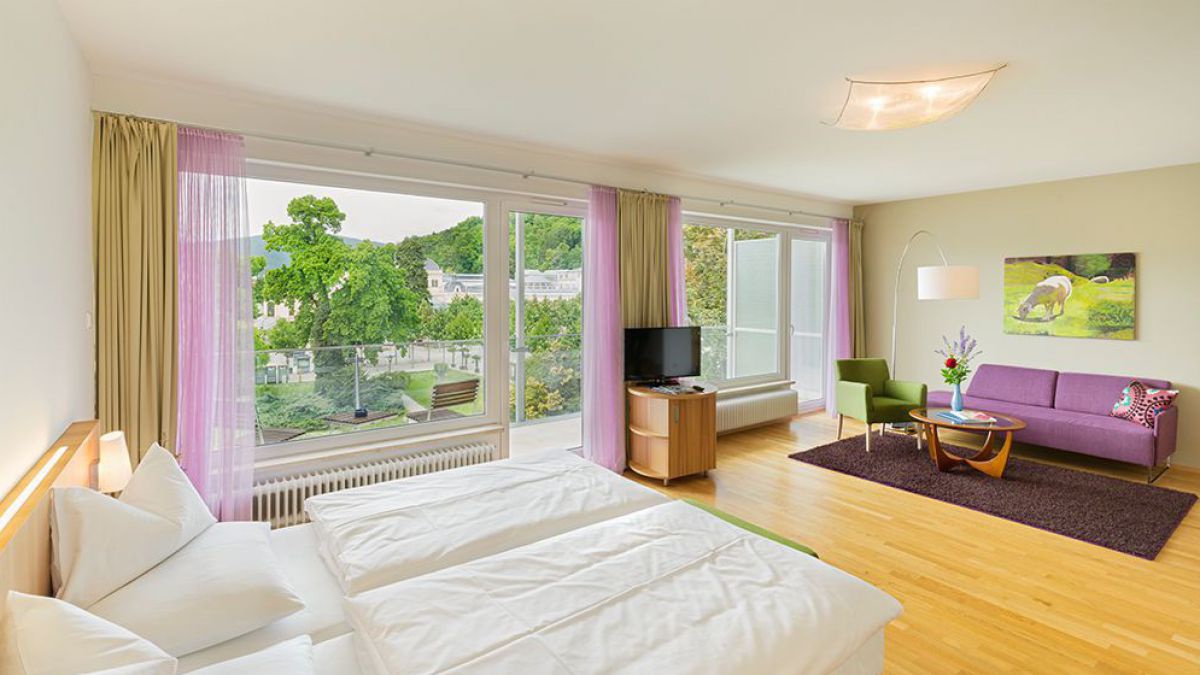 Zimmer in hellen Pastellfarben gehalten. Der Blick geht ebenfalls in den Park hinaus.