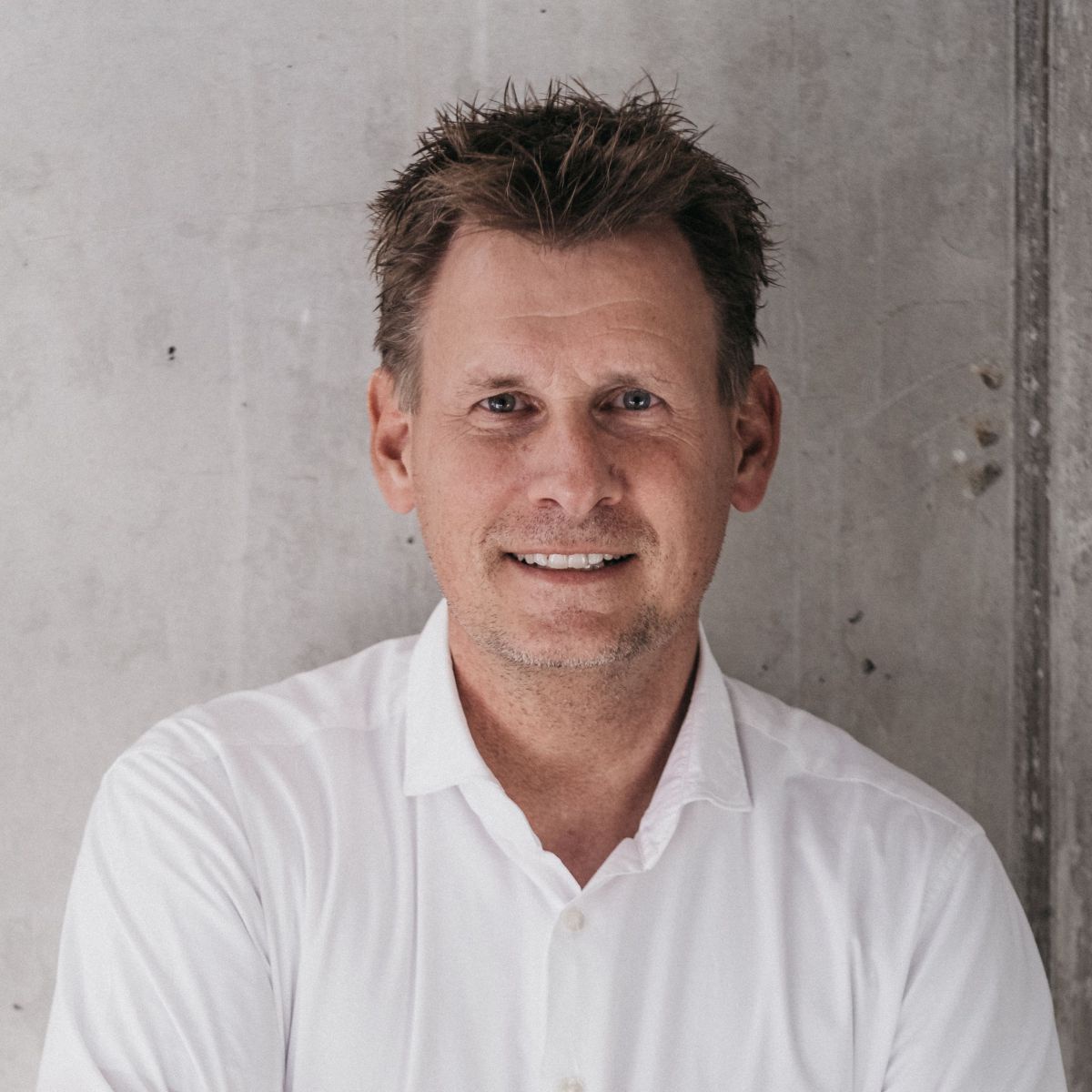 Herr Blumenkamp mit weißem Hemd vor einer Betonmauer.