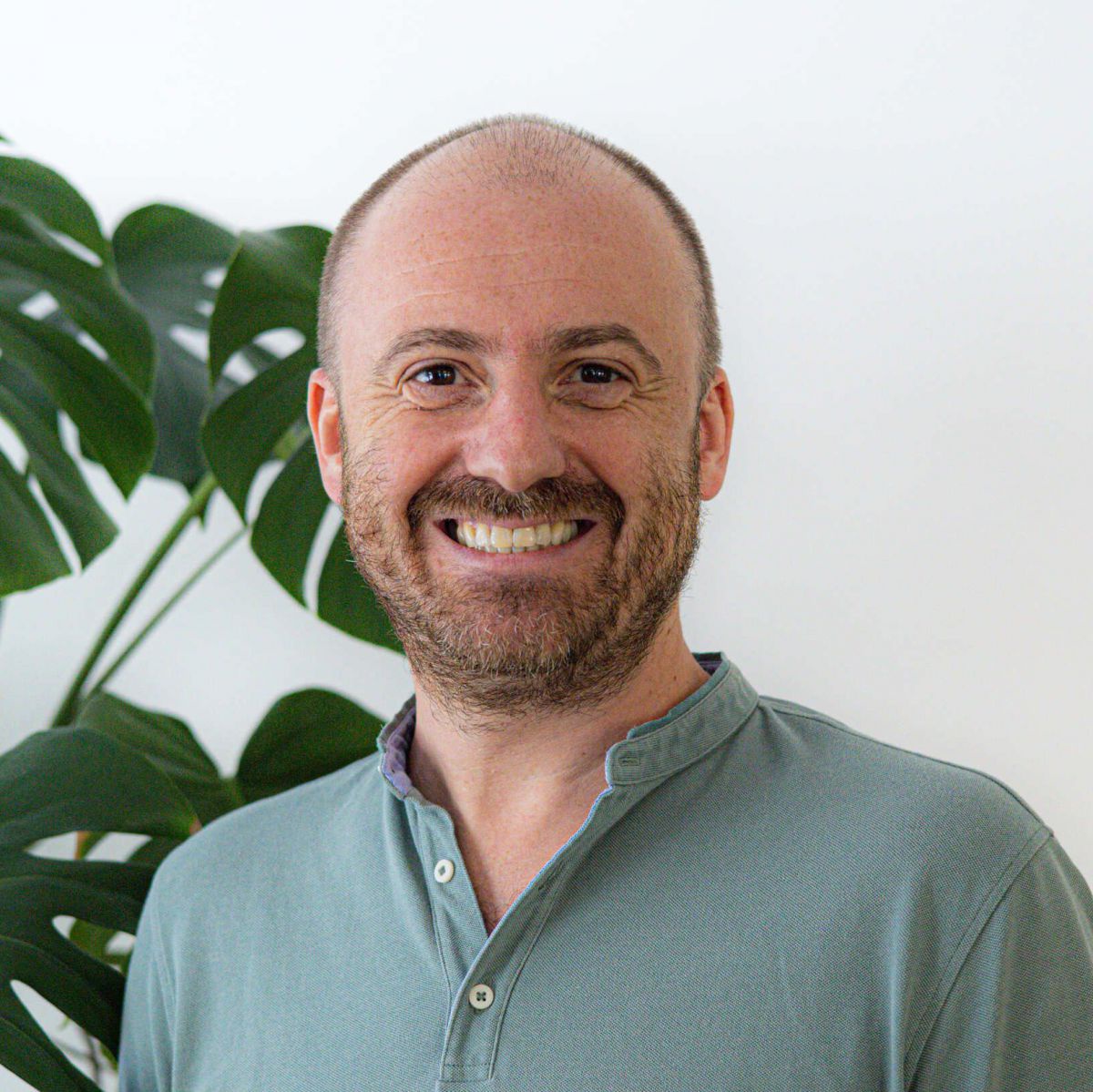 Herr Pfanner vor eine weißen Wand neben einer Monstera Zimmerpflanze.