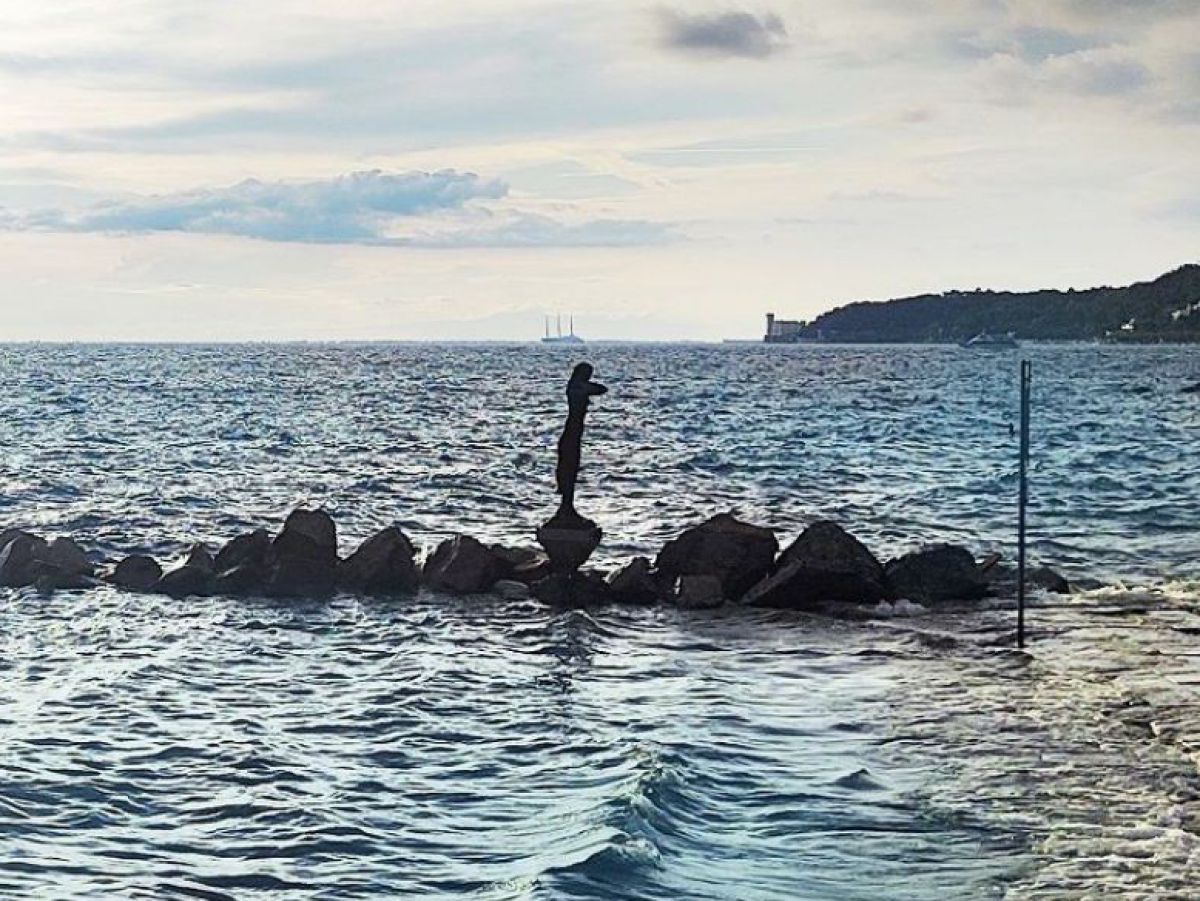 Blick aufs Meer, vom Ufer führt eine Reihee von Dteinmen ins Wasser. Auf einem Stein steht eine Statue.