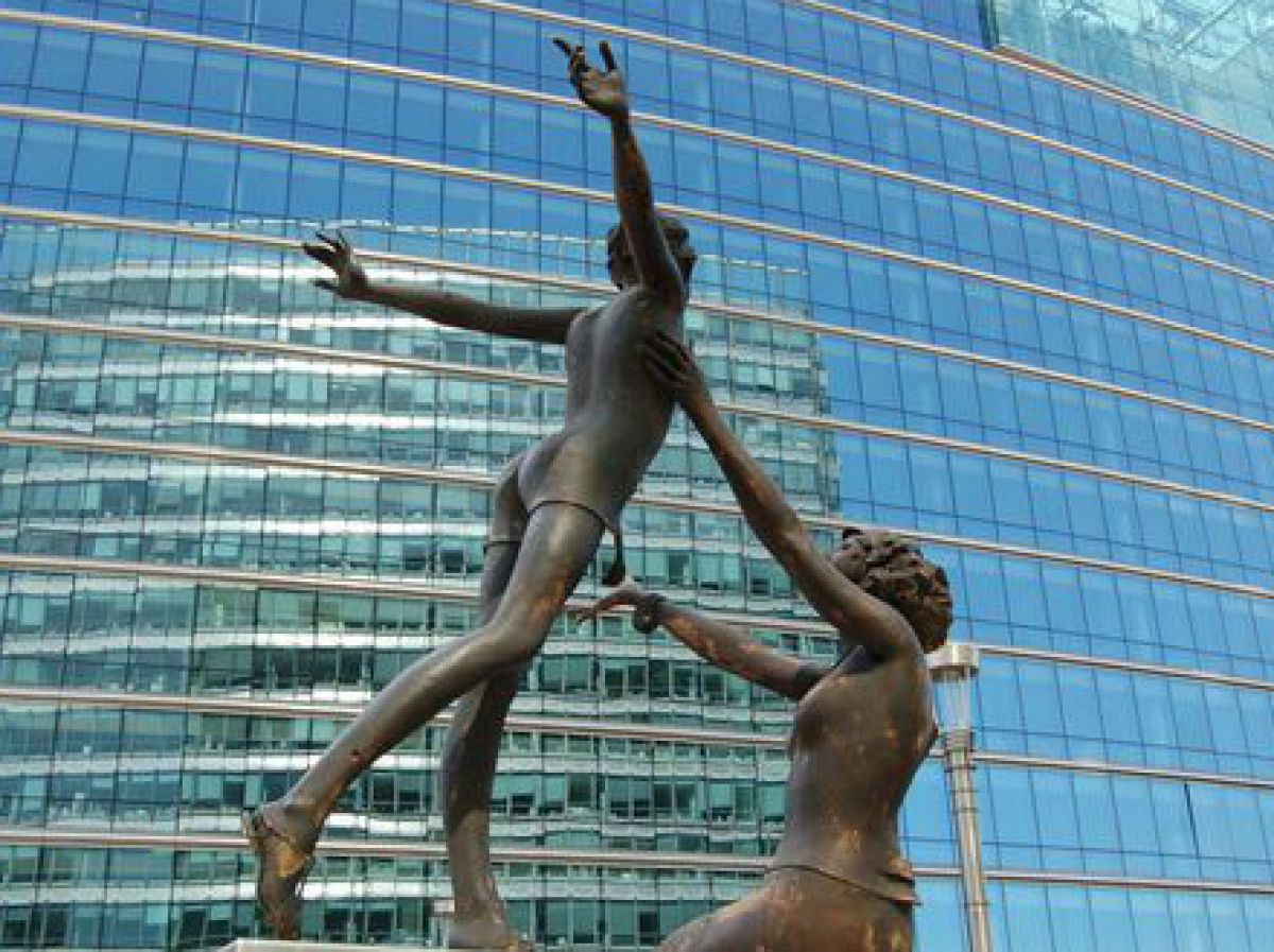 Statue tanzender Frauen vor der Glasfront eines Bürogebäudes.