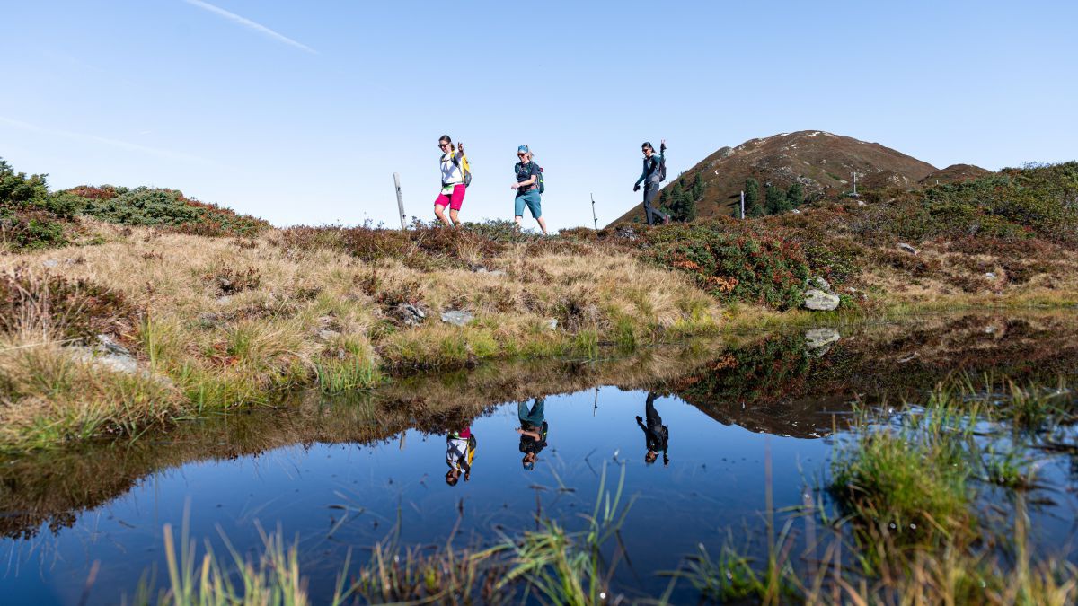Drei Personen wandern auf einem Grat entlang eines Bergsees.
