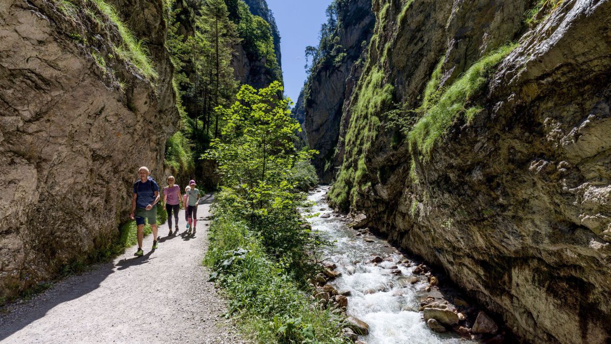 Eine Gruppe von Wanderern auf einem breiten Wanderweg, daneben ein Bach und links und rechts steile Felswände.