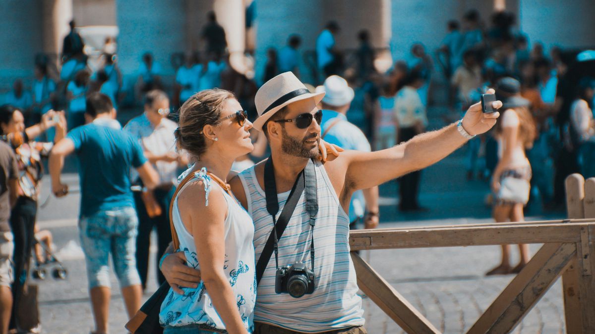 Mann und Frau machen ein Selfie auf einem belebten Platz mit vielen Touristen.