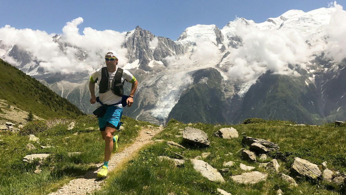 Läufer auf einem Weg in den Bergen, im Hintergrund ein schneebedecktes Bergmassiv mit Gletscher.
