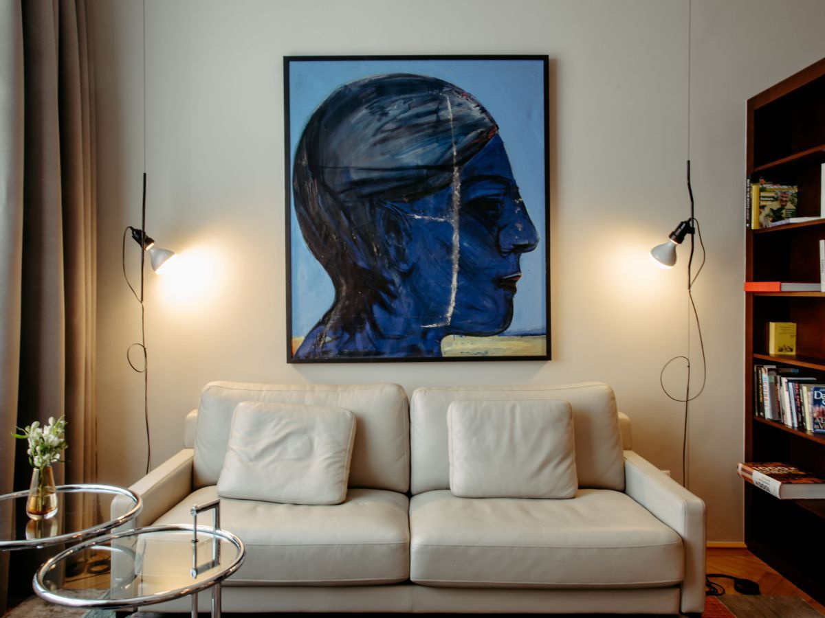 Sofa, Beistelltisch mit runden Glasflächen, an der Wand ein Gemälde: ein Kopf in blau gehalten.