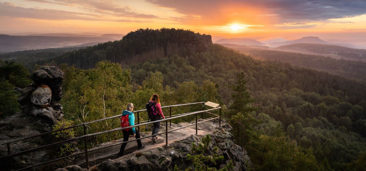 2 Personen auf einer Aussichtsplattform bei Sonnenuntergang.