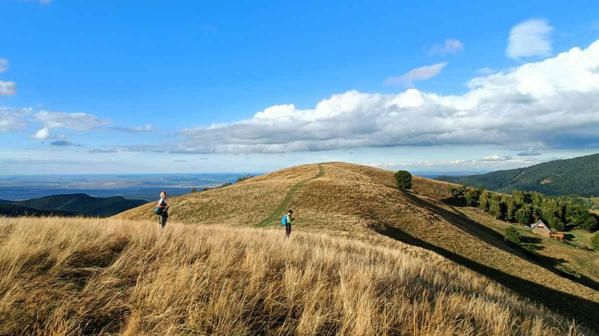 2 Personen auf einem hügeligen Wanderweg im hohen Gras. Extrem weite Fernsicht.