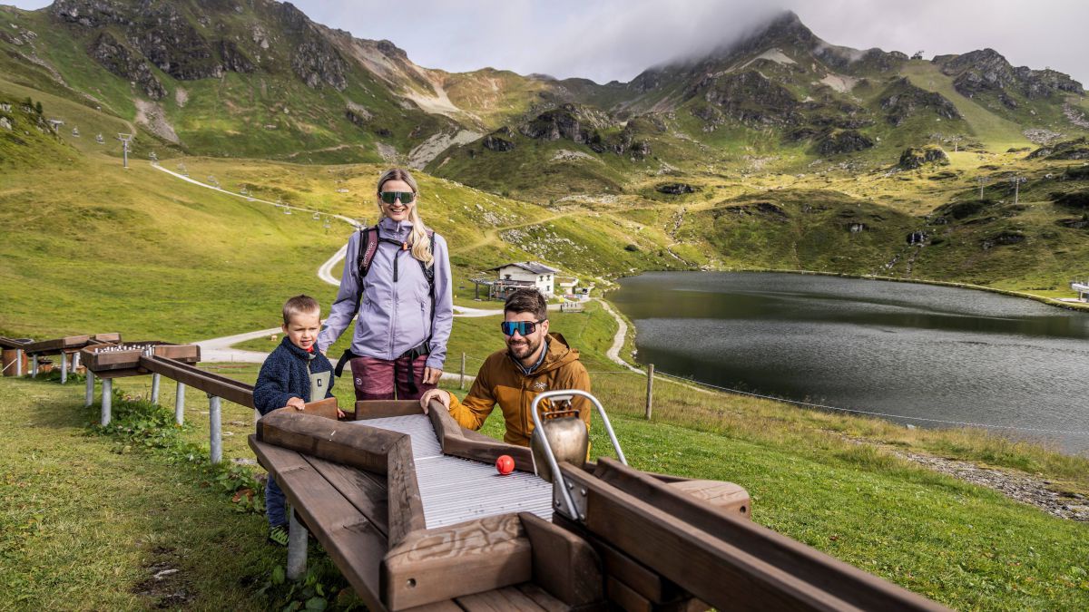 Mann Frau und Kind bei einer Kugelbahn an einem Bergsee.