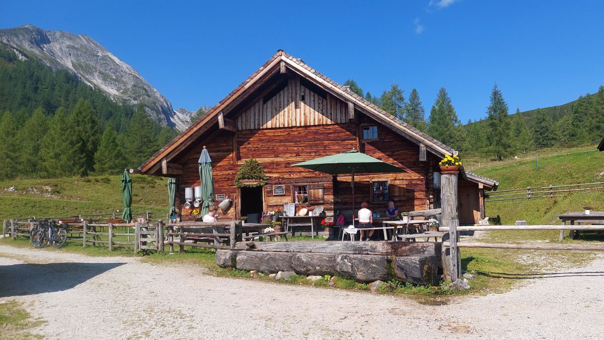 Almhütte, davor ein Sonnenschrim und Tische.