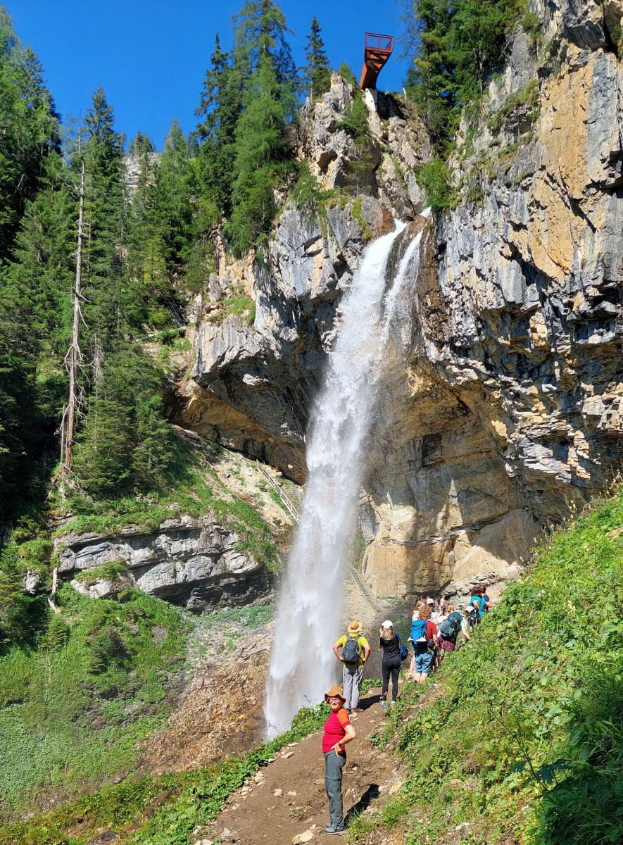 Wasser stürzt den Felsen runter, vor dem Wasserfall eine Wanderggruppe, darüber die Aussichtsplattform.