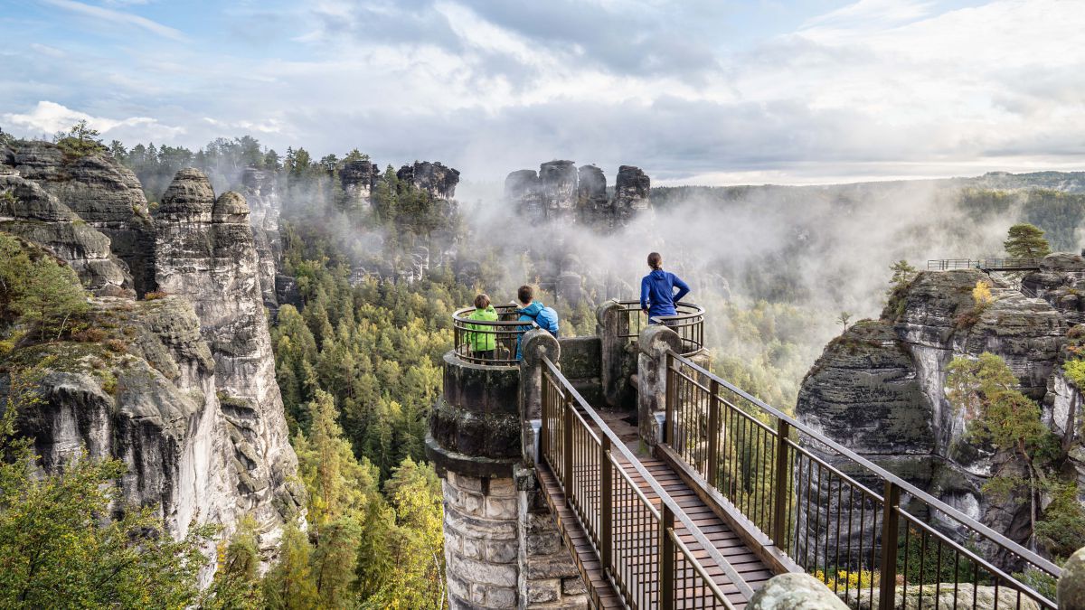 Auf einer Aussichtsplattform sind drei Personen. Blick auf die schroffe Felsenlandschaft.
