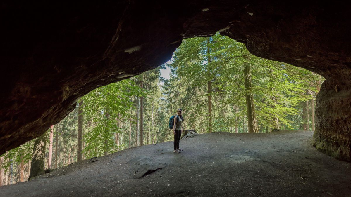 Blick von der Höhle raus in einen Wald. Am Eingang steht eine Frau.
