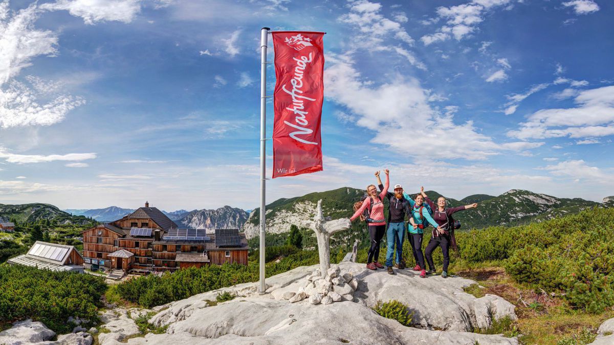 Fahne der naturfreunde und vier Personen auf einem Felsen davor.
