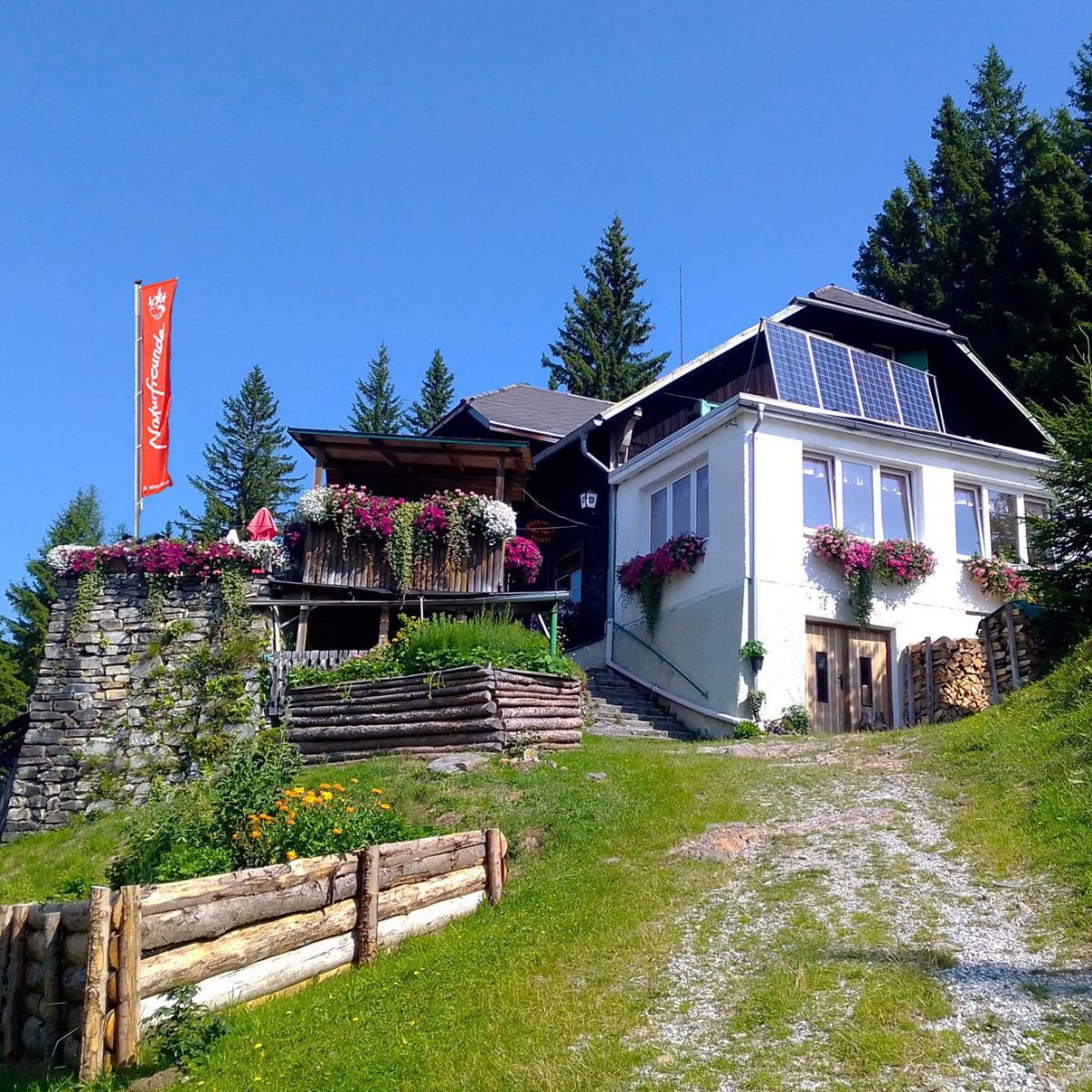 Unscheinbare kleine Hütte, davor eine Terasse und die Natorfreunde-Fahne.