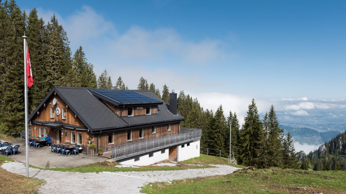 Berghütte aus Holz mit Blick ins Tal, in dem Wolkenfelder hängen.