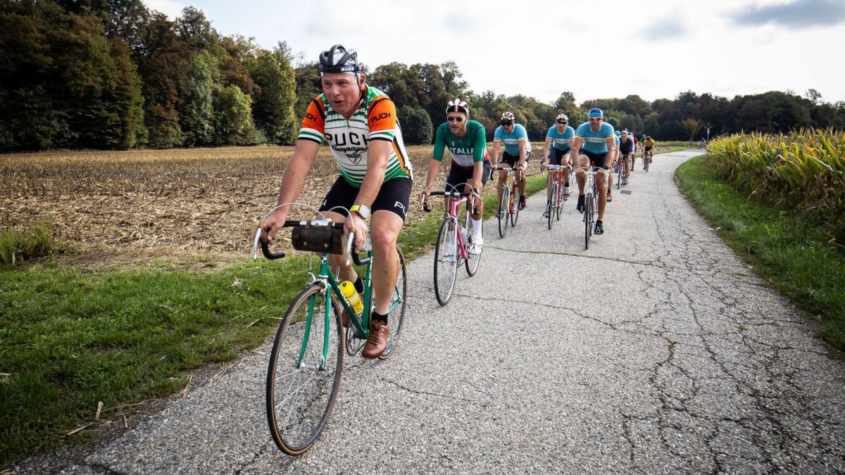Gruppe von Radfahrern auf einer schmalen asphaltierten Straße.