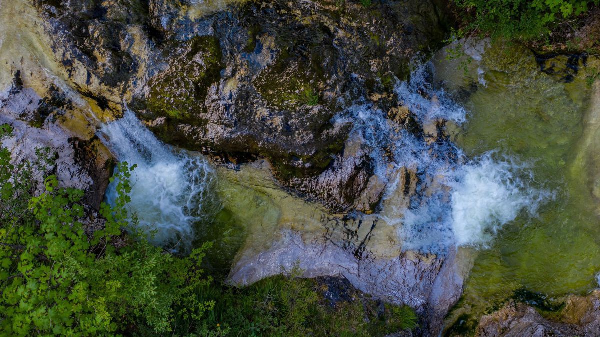 Blick von oben auf einen Wasserfall und See.