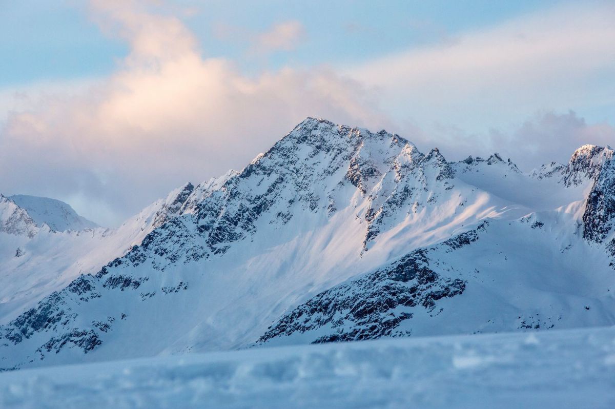 Schneebedeckte Bergspitzen unter einem wolkenverhangenen Himmel bei Sonnenauf- oder -untergang.