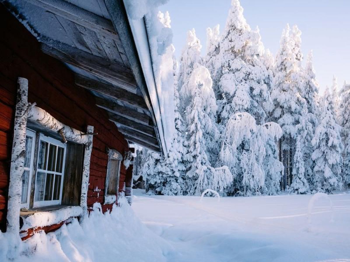 Rotes Holzhaus in einem tief verschneiten Wald.