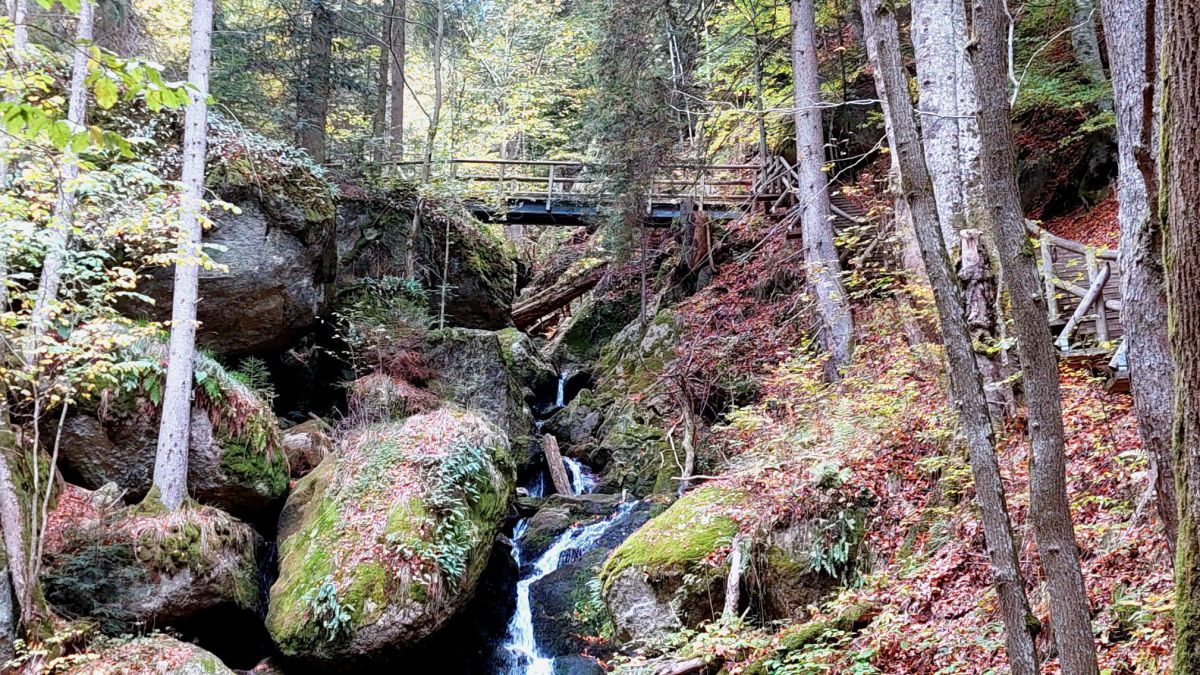 Wasser fließt zwischen Granitsteinenlinks ein Weh mit Holzstugen, der zu einer Brücke über die Klamm führt.