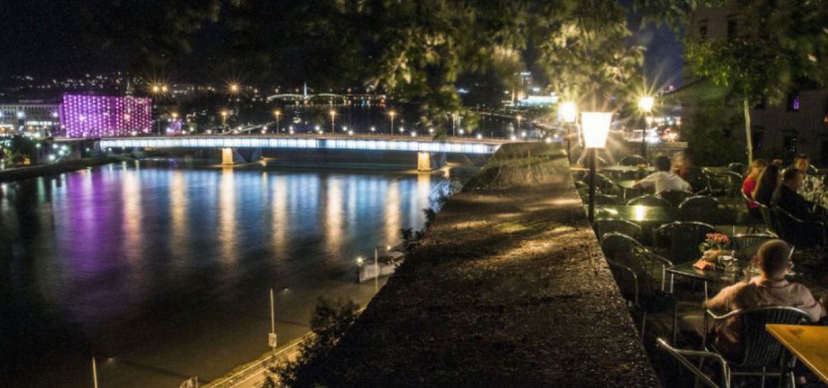 Blick vom nächtlichen Schlossberg auf das bunte Farbspiegelungen in der Donau